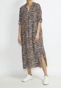 Lång, beige klänning med ett mönster av svarta zebraränder, knapplång framtill, rullade ärmar och hög sidoklyv. Kombinerad med vita sneakers.