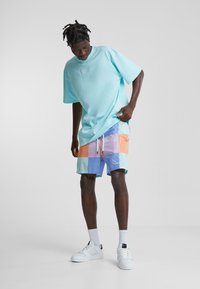 Light blue oversized t-shirt, colorful block-pattern swim shorts in pastel shades, white sneakers, and graphic detail on shorts.