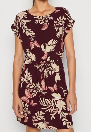 Woman wearing short-sleeve maroon dress with beige botanical and pink butterfly print, featuring a tie waist and round neckline.