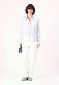 Light blue striped button-up shirt with two pockets, paired with white wide-leg pants and gray slip-on shoes, holding a small blue bag.