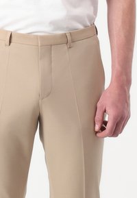 Pantaloni beige su misura con una texture liscia, vestibilità Slim, e dettagli delle tasche anteriori. Presentano passanti per cintura e una chiusura con zip classica.
