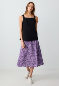 Top nero senza maniche con scollatura quadrata, abbinato a una gonna midi floreale viola. La modella indossa sneakers bianche. Design semplice e casual.