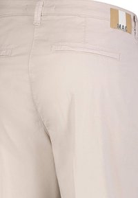 Beige katoenen broeken met een rechte snit, voorzien van twee achterzakken en een merklabel met verticale strepen in crème en goud.