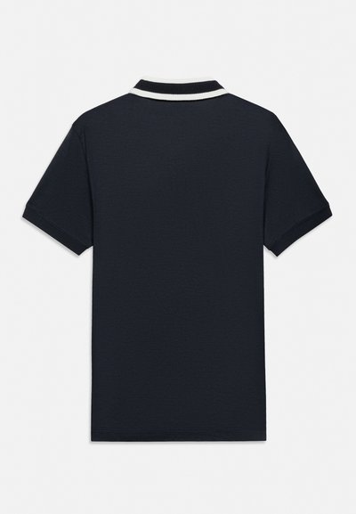 Kratka polo majica mornarsko modre barve z ovratnikom s belim robom, prikazana od zadaj na enobarvnem belem ozadju.