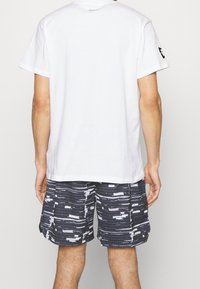 Hvid bomuld T-shirt med rund halsudskæring, parret med sorte shorts med et struktureret abstrakt mønster i hvide og grå striber.