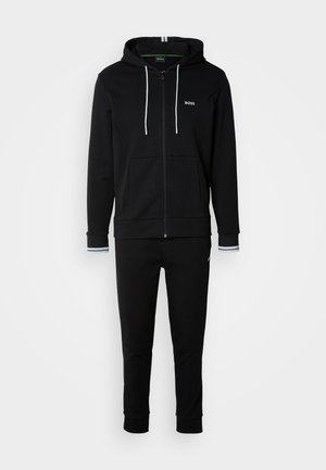 Felpa nera con zip, dotata di coulisse e tasche frontali, abbinata a pantaloni della tuta coordinati con polsini a coste e dettagli del logo.