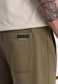 Olijfgroene sweatpants met een gladde textuur, een strak ontwerp, zijzakken en een zwart logo-label op de achterkant.