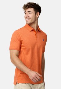 Polo-shirt orange en tissu texturé, avec une patte de boutonnage à trois boutons et un logo bleu sur la poitrine. Manches courtes avec une coupe ajustée.