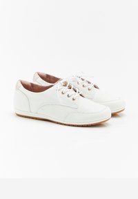 Scarpe bianche con lacci, dalla superficie texturizzata, occhietti dorati e suola di un beige chiaro. Materiale liscio con dettagli vicino al tallone.