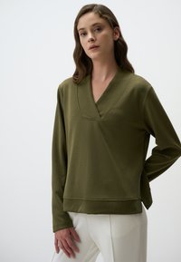 Maglietta a maniche lunghe verde oliva con scollo a V e vestibilità comoda, realizzata in materiale morbido. Presenta dettagli cuciti lungo il collo e l'orlo.
