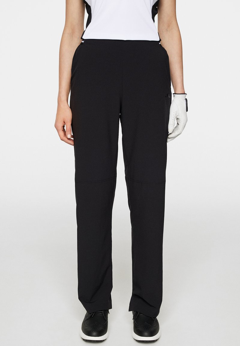 Svarta sportbyxor i lättviktsmaterial med avslappnad passform och minimalistisk design. Kombinerad med en vit överdel och svarta skor.