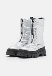 Srebrne puchate botki do kostki z podwójnymi zamkami błyskawicznymi, półmatową fakturą, masywną czarną podeszwą i logo na suwakach ułatwiającymi dostęp.