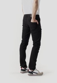 Pantalones cargo negros con múltiples bolsillos, ajuste ajustado, hechos de tela duradera. Combinados con zapatillas blancas y grises, que muestran un diseño deportivo.