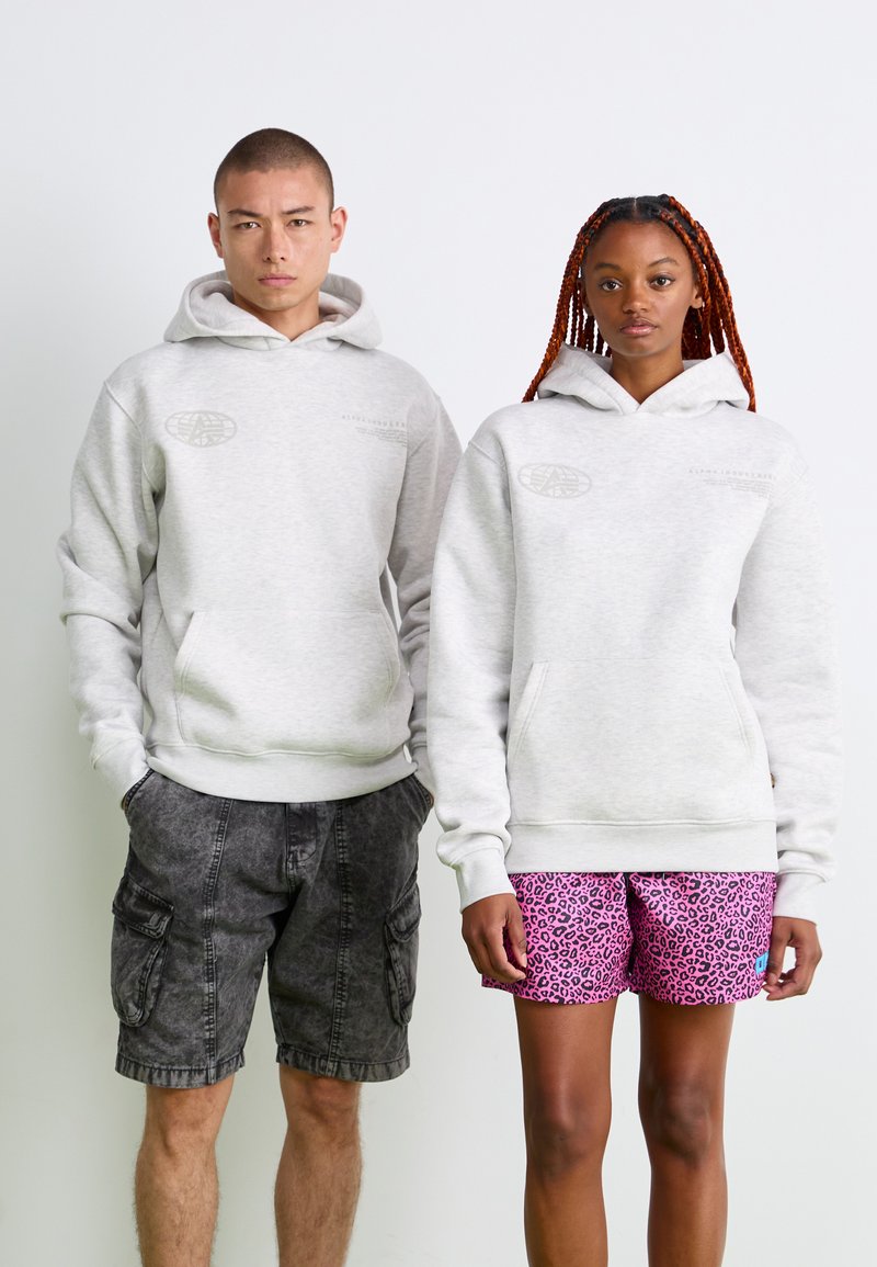 Lys grå hættetrøjer med forlommer og logoer. En person har mørke cargo-shorts på, mens den anden har lyserøde shorts med leopardmønster.