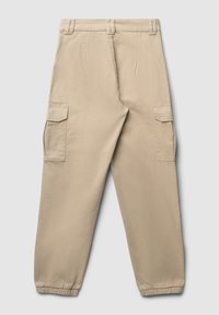Beige Cargo-Hosen mit lockerer Passform, elastischen Bündchen, zwei Seitentaschen und je einer Klappentasche an jedem Oberschenkel. Hergestellt aus weichem Baumwollstoff.