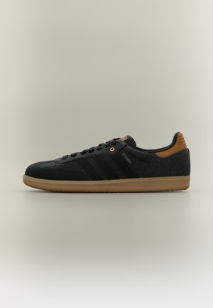 Scarpa da ginnastica Adidas Samba nera e grigio scuro con suola in gomma, linguetta posteriore marrone e lacci neri, vista laterale su sfondo chiaro.