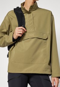 Olivově zelená mikina s vysokým límcem, předním kapesním a logem H/H. Má hladkou, matnou texturu a černý nastavitelný ramenní popruh.