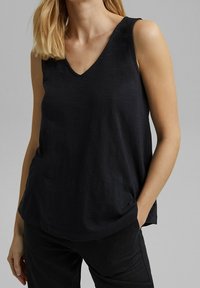 Svart ärmlös topp med V-ringning, tillverkad av lätt tyg. Har en avslappnad passform och subtila texturerade detaljer vid axlarna.