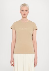 Béžové bavlněné tričko s krátkými rukávy, na přední straně s bílým textem "Armani Exchange Milano/New York". Hladký povrch, klasický střih.