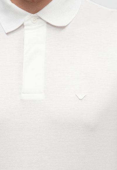 Bílé polo tričko s texturovaným límcem, zapínáním na dva knoflíky a malým vyšitým logem na hrudi. Hladká bavlněná látka.
