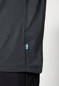 Schwarzes Stoffhemd mit strukturierter Oberfläche, ausgestattet mit einem kleinen blau-gelben schwedischen Flaggenetikett am Saum und kontrastierenden Nähten.