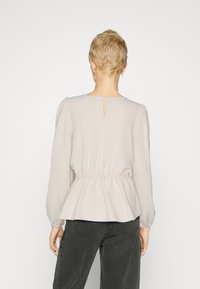 Light gray blouse with long sleeves, elastic waist, and keyhole opening at the back. Made from a soft, textured fabric.