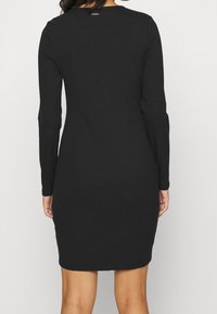 Robe noire à manches longues côtelée, présentant un col rond et une silhouette simple et ajustée. Texture lisse sans motifs ni accents visibles.