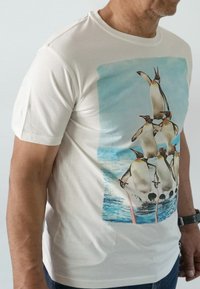 Korte mouw witte t-shirt met een kleurrijke afbeelding van pinguïns tegen een blauwe oceaan achtergrond. Zacht materiaal met een relaxte pasvorm.