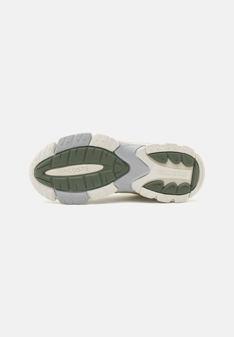 Suela de zapatilla Lacoste en gris y crema con acentos verdes. Presenta goma texturizada para agarre y durabilidad, con elementos curvados y marca.