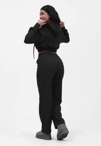 Sudadera negra corta con cordones, combinada con pantalones negros holgados que tienen bolsillos. Footwear gris complementa el atuendo. Textura simple.