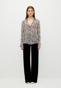 Blusa floral con una tela ligera y transparente en colores azul marino y crema, con botonera y mangas largas, combinada con pantalones de pierna ancha negros.