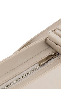 Borsa in pelle beige con una texture liscia, dotata di una cerniera superiore e un cursore in metallo. Il design presenta un profilo snello e una tracolla regolabile.