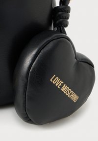 Μαύρη δερμάτινη τσάντα με σχήμα καρδιάς ως διακοσμητικό. Διαθέτει χρυσό κείμενο "LOVE MOSCHINO" και υφή επιφάνειας. Οι λαβές είναι κόμπες για λεπτομέρεια.