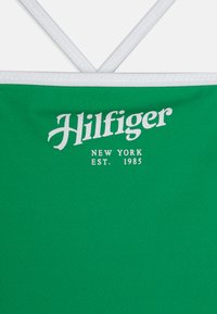 Débardeur vert sans manches avec bord blanc, arborant le logo "Hilfiger" et "New York EST. 1985" imprimé en blanc sur le devant.