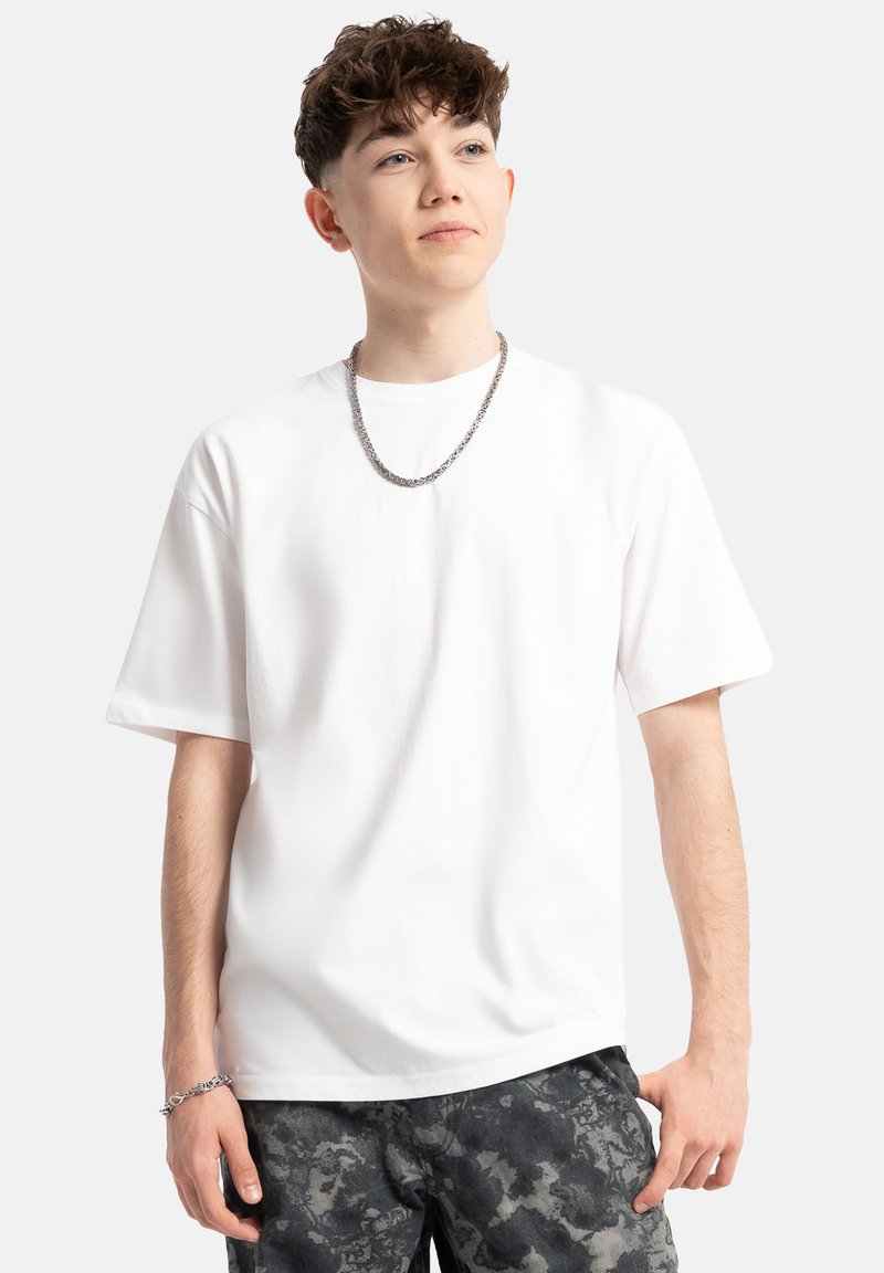 Biała bawełniana koszulka z krótkim rękawem i okrągłym dekoltem. Dopasowana do ciemnych, wzorzystych szortów, uzupełniona srebrnym naszyjnikiem.