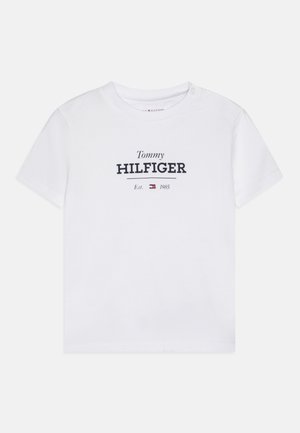 Camiseta blanca de algodón con mangas cortas, que presenta el texto "Tommy HILFIGER" en azul marino, junto con un pequeño logotipo y la fecha de fundación debajo.