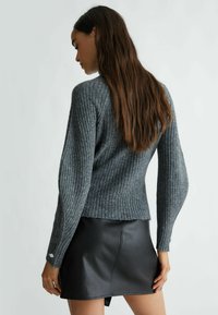 Maglione grigio a coste con maniche lunghe, motivo a maglia testurizzato e orlo corto. Abbinato a una minigonna in pelle nera.