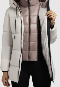 Chaqueta acolchada con una capa exterior de un gris claro, que cuenta con capucha y cremalleras negras. En el interior, un chaleco acolchado ajustado de color malva con diseño de acolchado cuadrado.