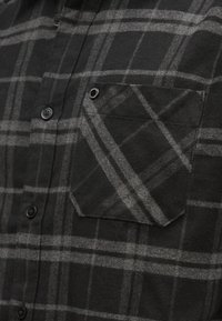 Camisa xadrez preta e cinza, de manga comprida, com gola arredondada, botões pretos e bolso de aplicação no peito esquerdo.