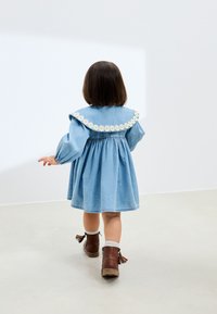 Robe en denim avec un large col fleuri brodé et des manches bouffantes, associée à des bottines marron à glands.