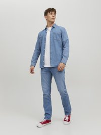 Camisa de mezclilla en azul claro con dos bolsillos en el pecho, camiseta blanca debajo, jeans azul claro y zapatillas rojas con suelas blancas.