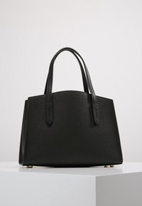 Czarna skórzana torba typu tote o wyraźnej konstrukcji, z krótkimi uchwytami, teksturowaną powierzchnią i stabilizującymi nóżkami w kolorze złotym.