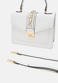Hvid quiltet taske med guldkæde, sort kant og en metallisk spænde. Inkluderer en aftagelig skulderrem.
