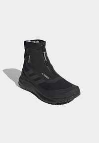 Chaussure de sport montante noire avec fermeture éclair frontale, semelle texturée et marquage Terrex sur le côté et la languette.