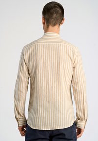 Camicia a maniche lunghe beige e bianca a righe con colletto, polsini con bottoni, tessuto leggermente texturizzato e orlo arrotondato. Vista dal retro.