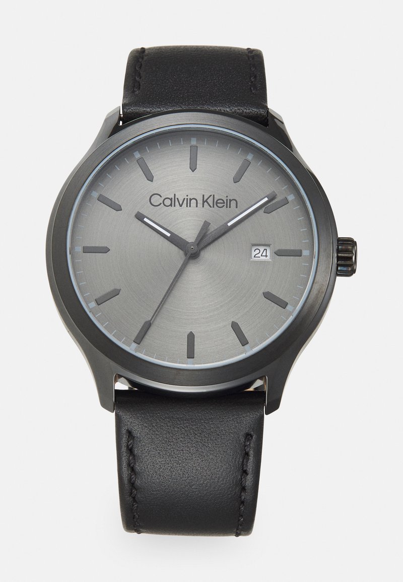Reloj de pulsera Calvin Klein con una esfera gris, marcadores de hora negros y una pantalla de fecha. Presenta una correa de cuero negro y una caja redonda lisa.