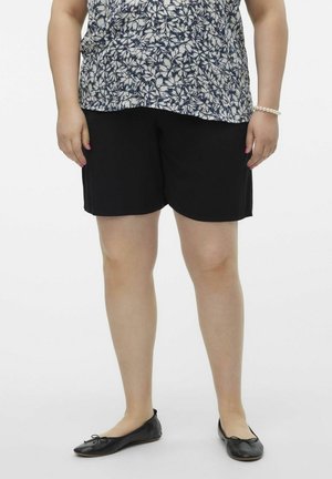 Zwarte shorts met een ontspannen pasvorm, gecombineerd met een bloemenblouse. De draagster heeft ook zwarte balletpumps en een parel armband.