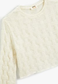 Maglione lavorato a maglia off-white con un motivo testurizzato, maniche lunghe e scollatura rotonda. Presenta una lunghezza leggermente accorciata e un orlo sfilacciato.