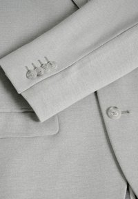Light grey tailored jacket showing a smooth texture. Four transparent buttons on cuff with a sleek design. Patch pocket visible.
