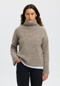 Világosbarna gyapjúkeverék garbó pulóver laza fazonnal, bordázott mandzsettákkal és puha, texturált felülettel. Sötét farmerrel párosítva.